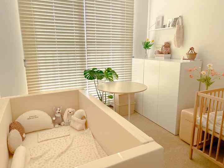 柔らかなベージュとナチュラルな木目調の赤ちゃん部屋、バンパーベッドとベビーベッド、ホワイトの収納が配置された雰囲気のあるインテリア