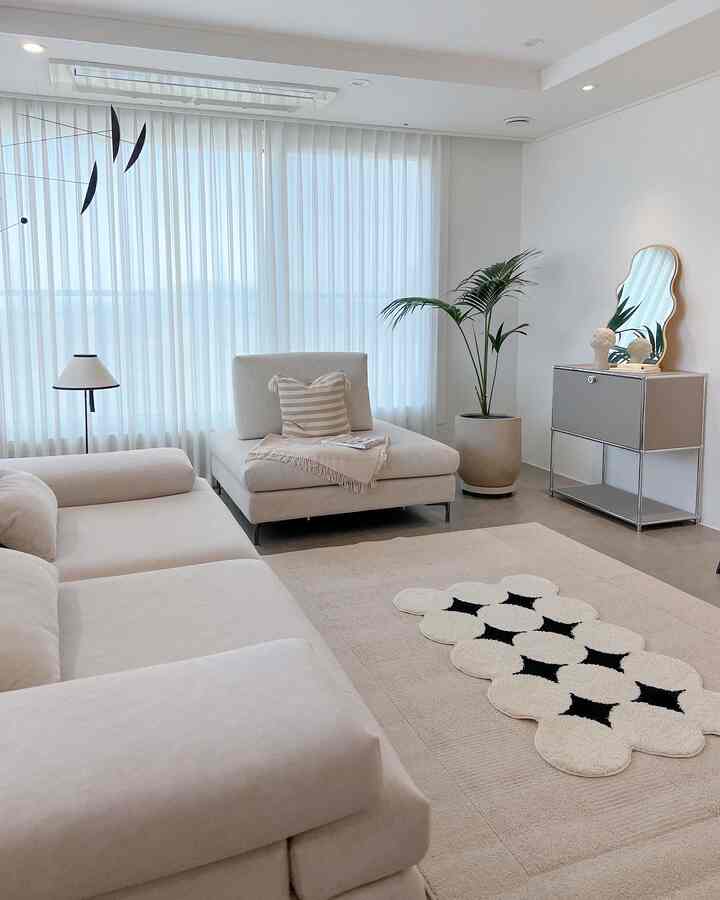 White and beige toned living room featuring a simple modern sofa and rug with a plant adding natural accent