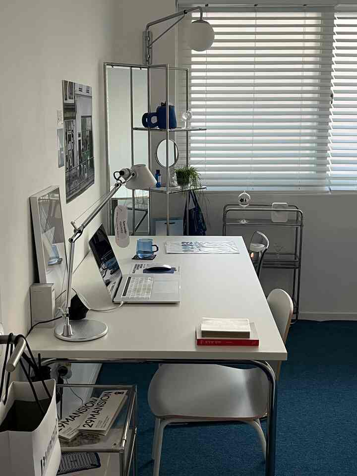 White and blue toned studio apartment home office featuring a large desk and office chair centrally arranged with minimalistic decor