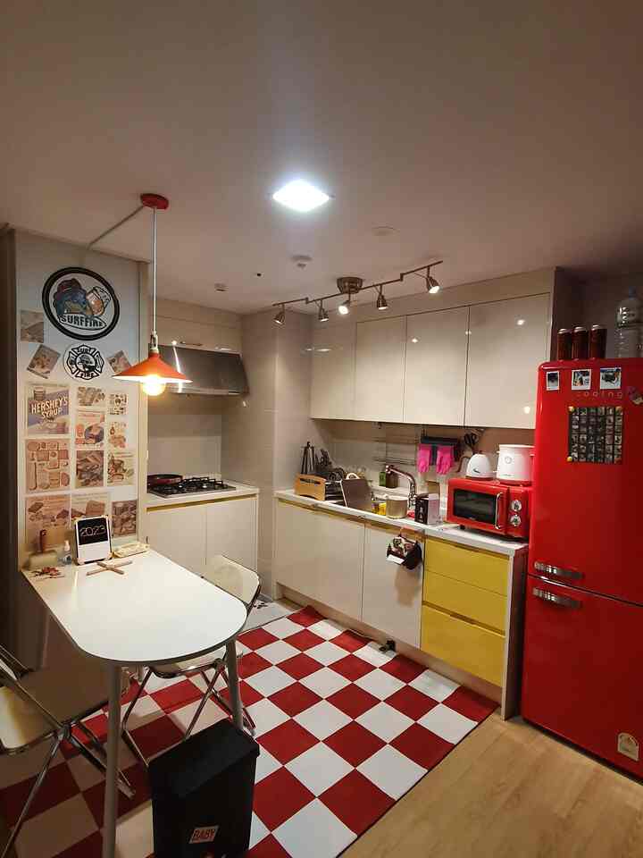 赤と白の色調のワンルームキッチン、レトロな冷蔵庫とチェッカーボード柄の床が印象的な居心地の良い空間