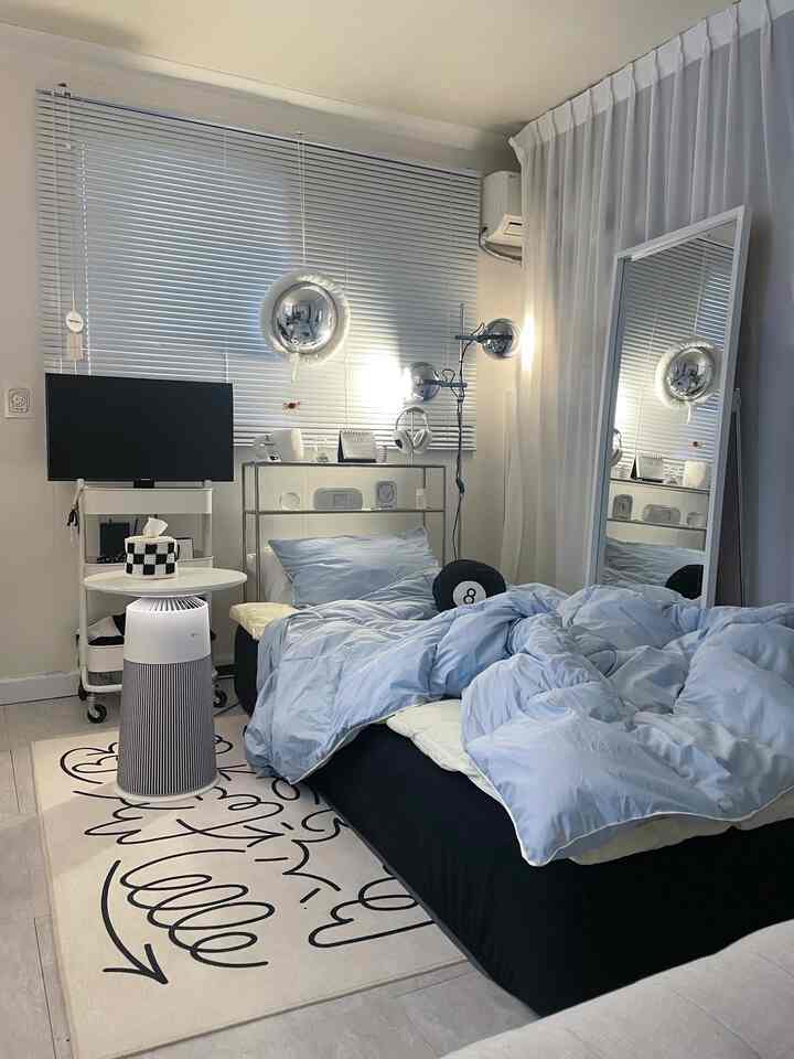 A modern single household bedroom dominated by white and black tones, featuring blue bedding, a large mirror, and aluminum blinds