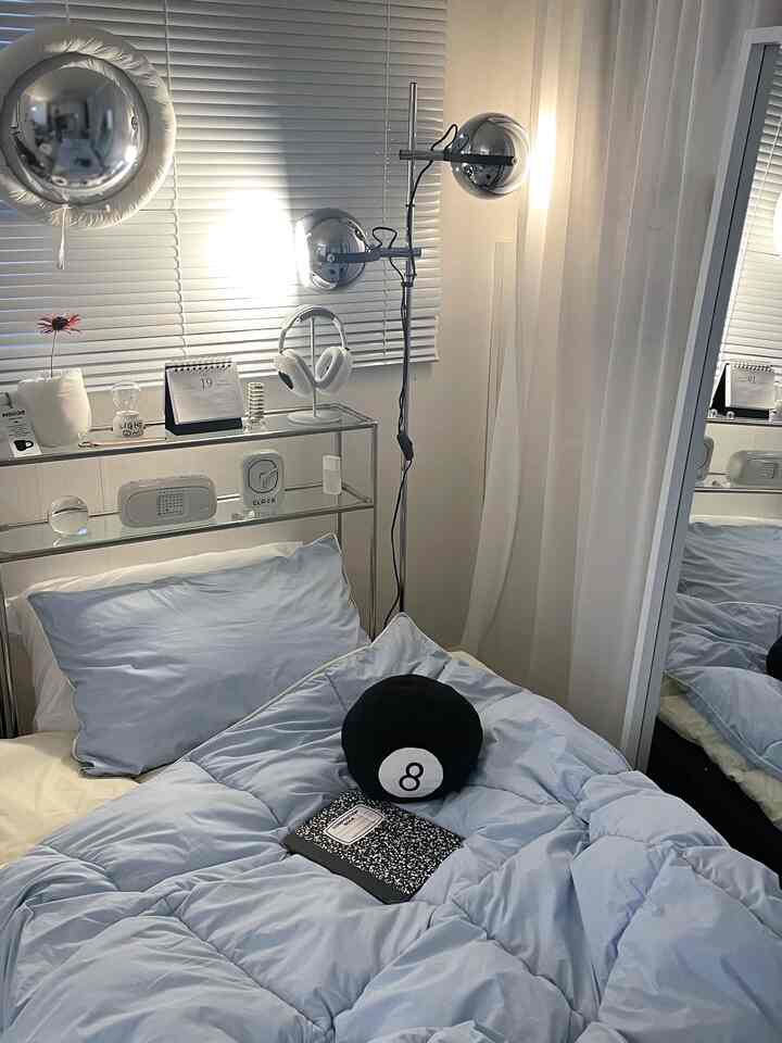 A white and blue toned bedroom featuring neat bedding and a metallic floor lamp in a minimal and modern setting