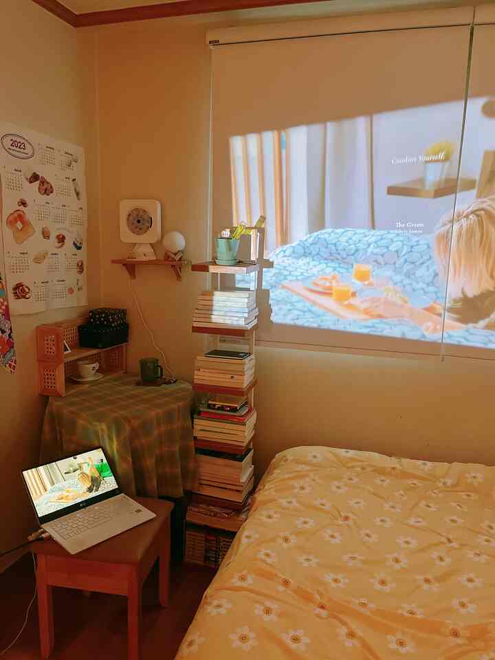 Cozy bedroom with yellow floral bedding and wooden furniture in a compact space, featuring a projector screen on the wall conveying a home cinema vibe