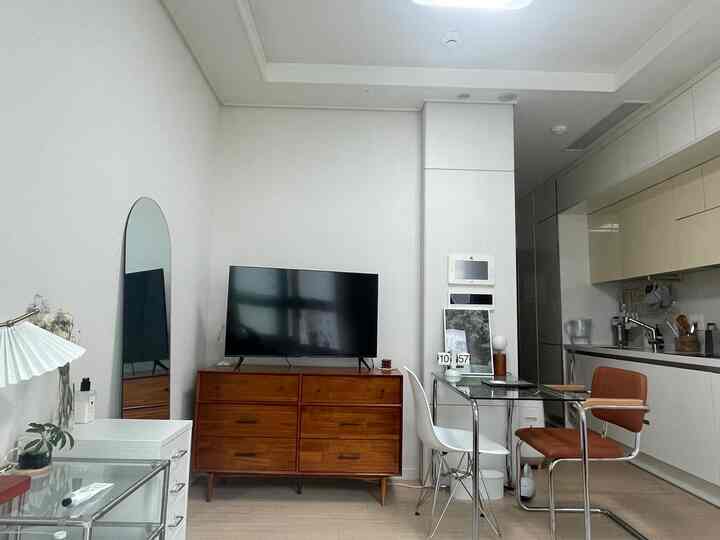 明るいホワイトとブラウンのトーンのワンルームリビング兼ダイニング、ミッドセンチュリーモダンの木製テレビ台とガラスダイニングテーブルが調和した印象的なインテリア