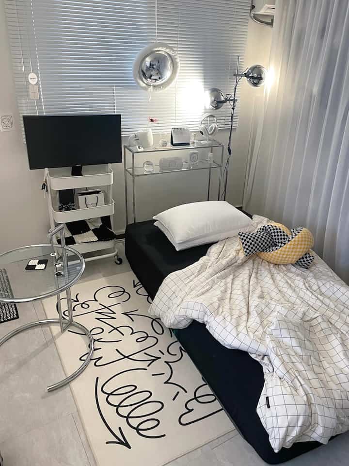 Modern studio bedroom in black and white tones featuring a mattress with pillow, stylish rug, and aluminum blinds