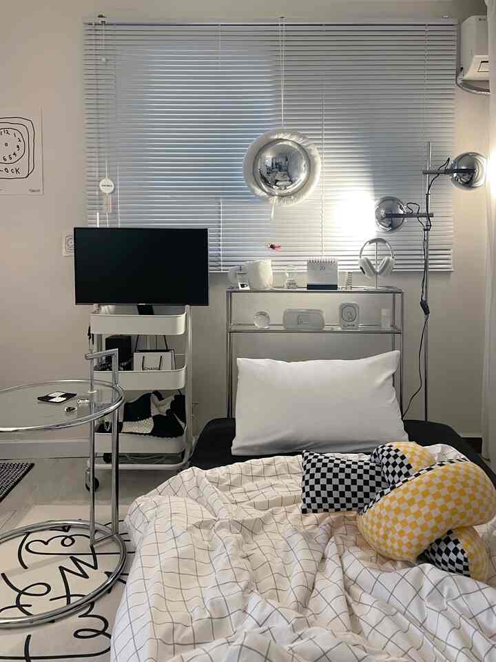 White and metallic toned bedroom featuring modern console, blinds, pillows, and cushions in a tidy space