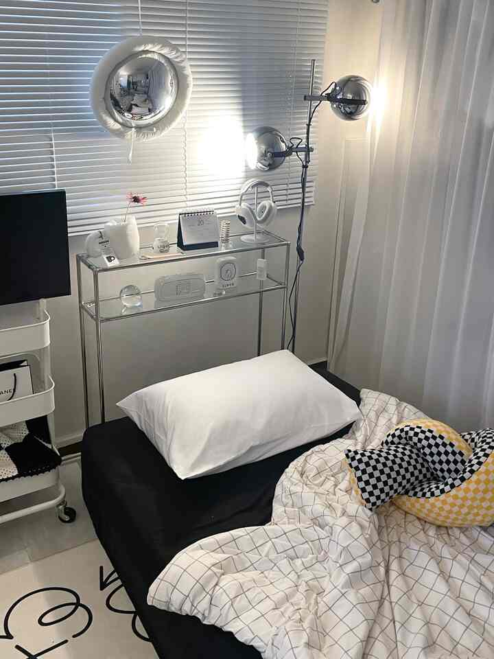 Modern and minimal bedroom in white and black tones featuring a bed with pillow, blinds, and metallic lighting fixtures