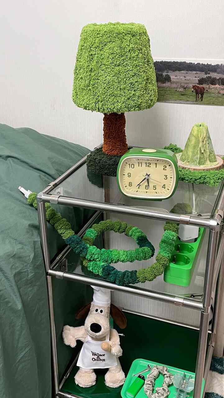 緑色のトーンの寝室、メタルフレームの棚に緑のテーブルランプとレトロな時計、キャラクターのぬいぐるみが配置された落ち着いた雰囲気のインテリア