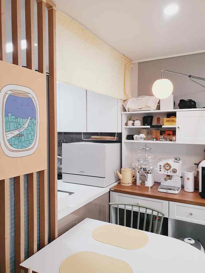 白とベージュのトーンでまとめられたコンパクトなキッチン、おうちカフェのコーヒー機器とダイニングテーブルが配置された雰囲気のある空間