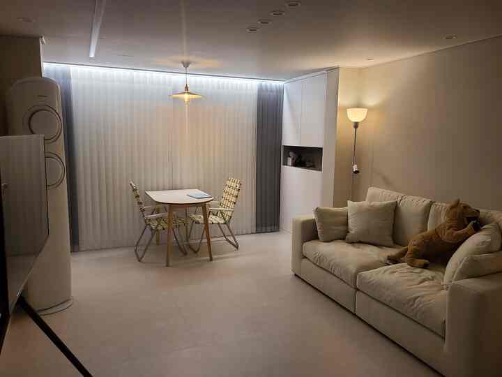 Bright white and natural wood tone 24-pyeong living room with a sofa and two-person dining table in a cozy newlywed home interior