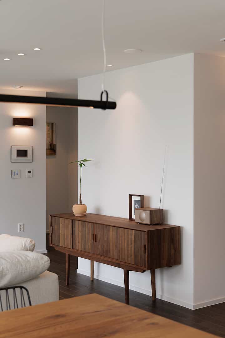 白い壁とウォールナット製の木製キャビネットが配置されたモダンで雰囲気のあるリビングルーム