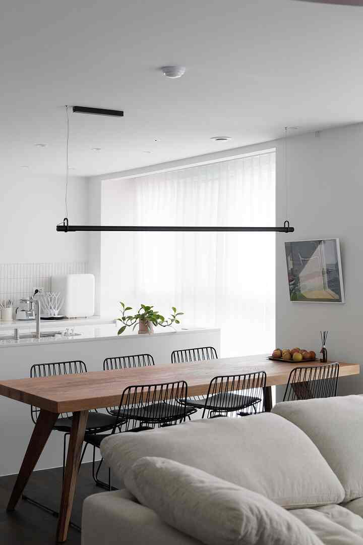 A simple dining room in white and wood tones, featuring black dining chairs and a pendant light creating a modern atmosphere