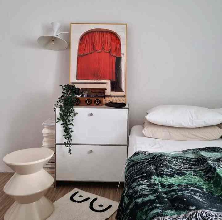 Bright white and beige bedroom featuring a storage cabinet and wall sconce with a clean, natural ambiance