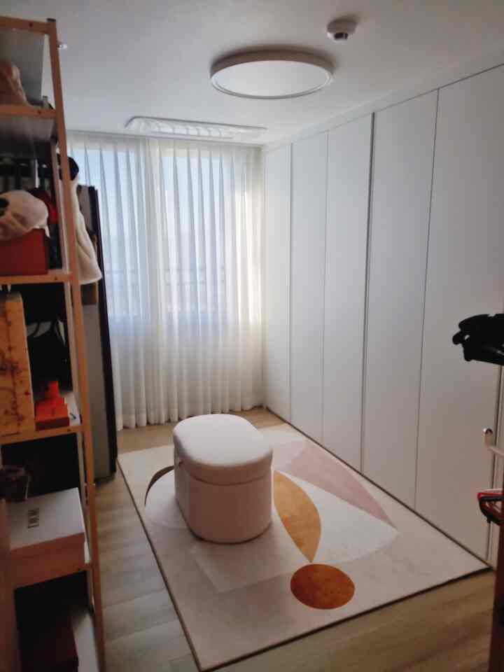 White and beige toned walk-in closet featuring curtains and a stool in a cozy small space