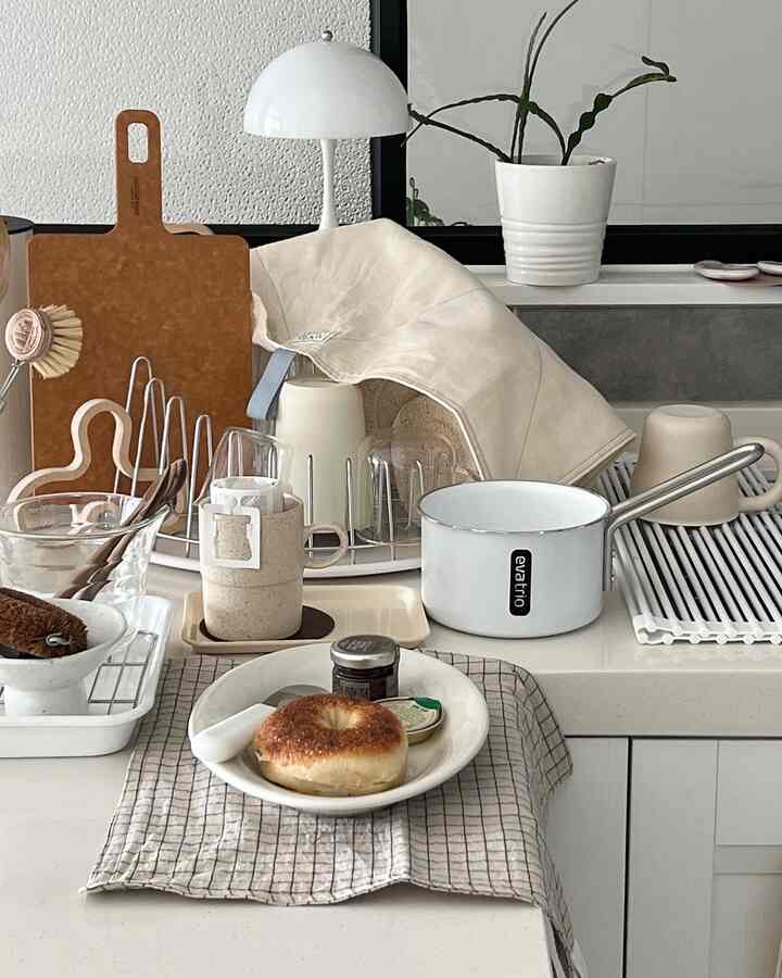 A white and beige toned kitchen space featuring assorted kitchen utensils, trays, and a pot on a clean countertop with cozy atmosphere