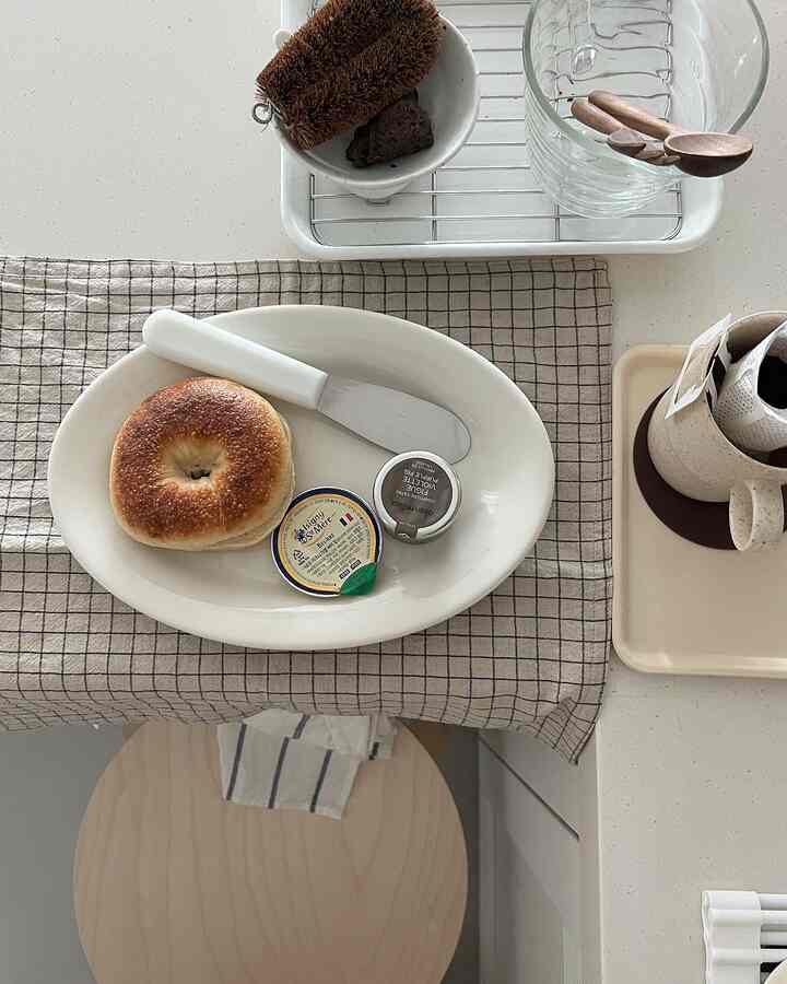 Natural beige-toned kitchen featuring bagel on plate, wooden spoons, and clean warm atmosphere