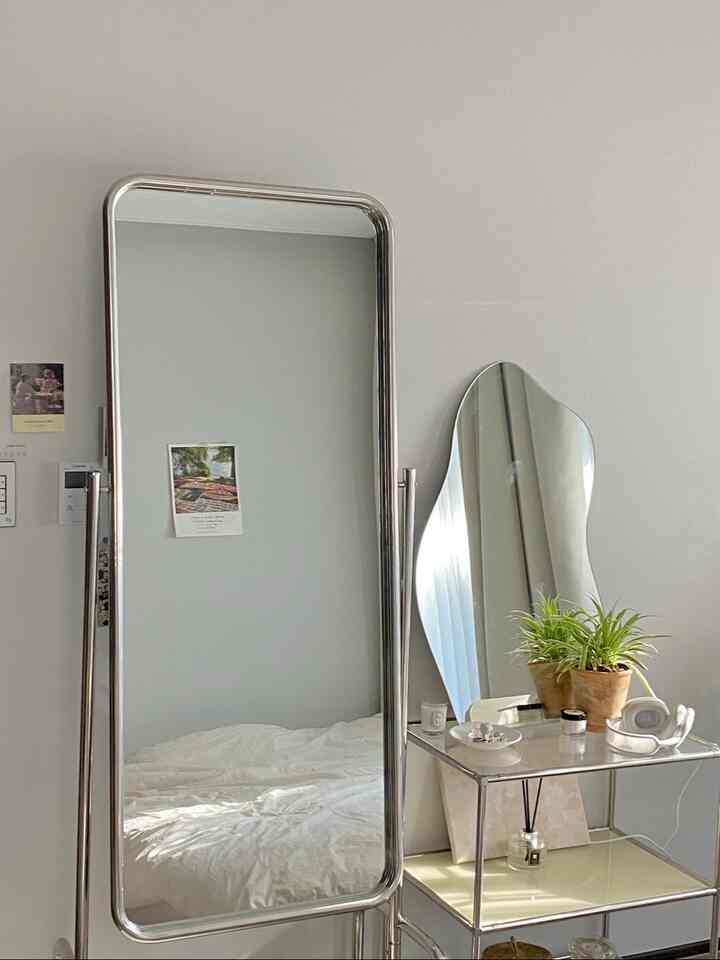 白い壁とベッドリネン、シルバーの金属フレームミラーと棚が配置されたミニマルなウォークインクローゼットの印象的な空間