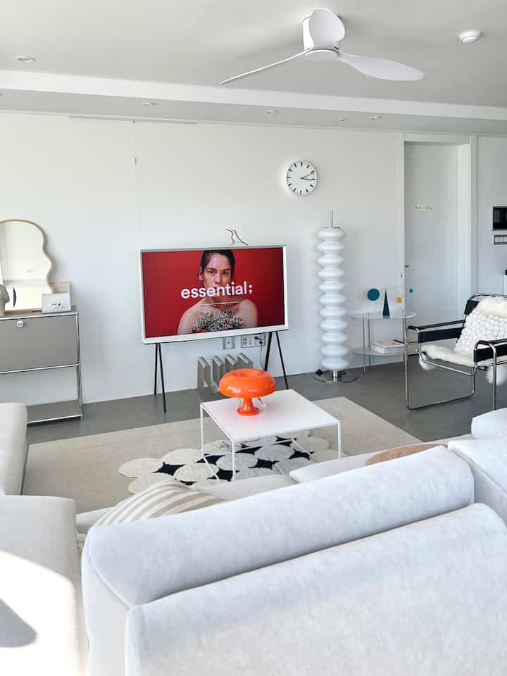 明るいホワイトトーンのリビング、中央に白いソファとオレンジ色のテーブルランプが配置された印象的なミッドセンチュリーモダンインテリア