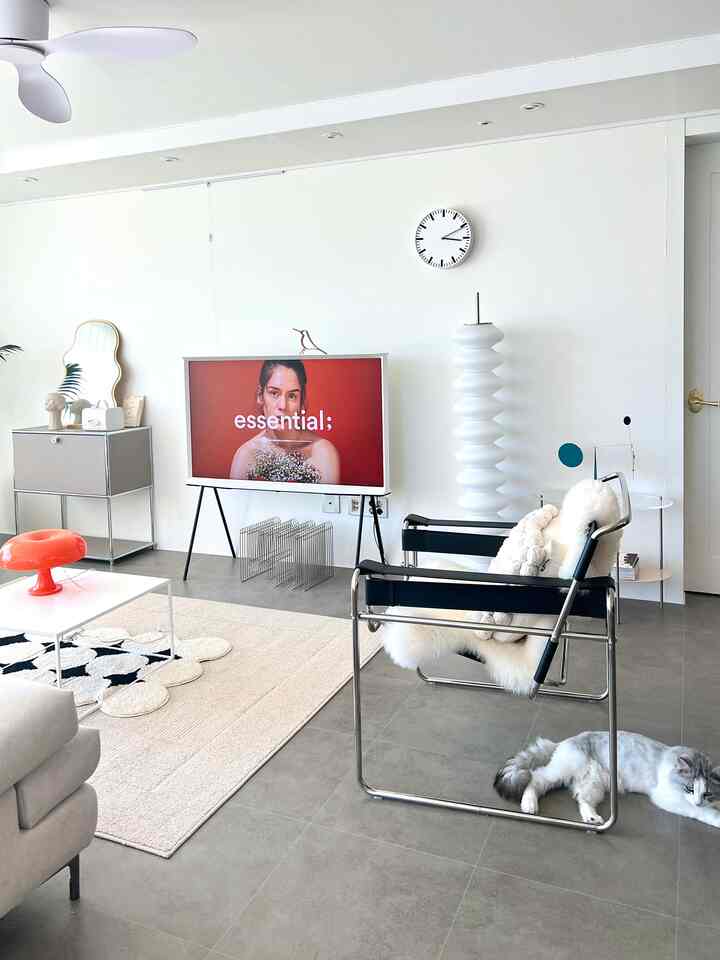 Bright white and gray toned living room featuring modern armchair, TV stand, and rug in a clean space