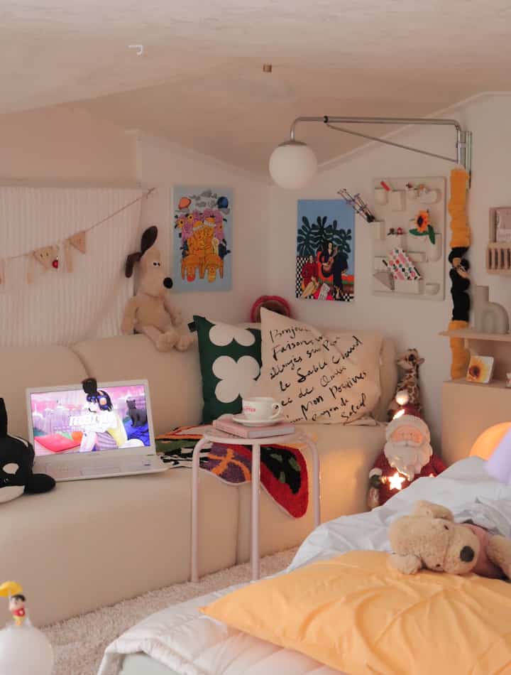 明るいベージュ色調のロフト、居心地の良いソファとクッション、壁照明、コーヒーカップが調和した雰囲気のあるインテリア