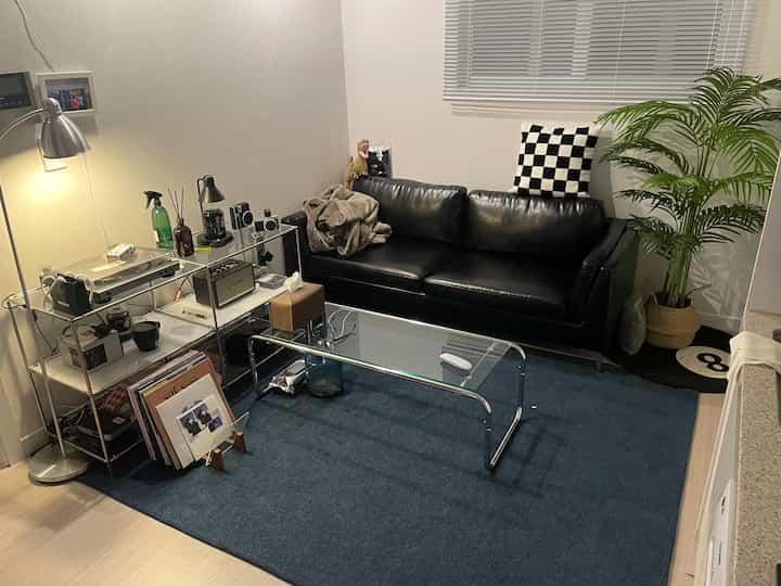 モダンなリビング、黒のレザーソファとネイビーのラグが配置され、金属とガラスの家具が洗練された雰囲気を演出