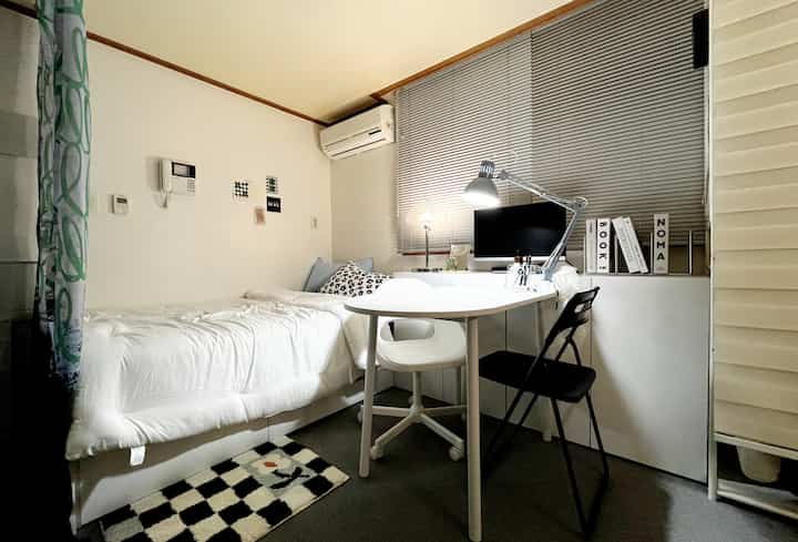 Small studio apartment bedroom in white and gray tones, featuring bed and desk arranged in a cozy, efficient layout
