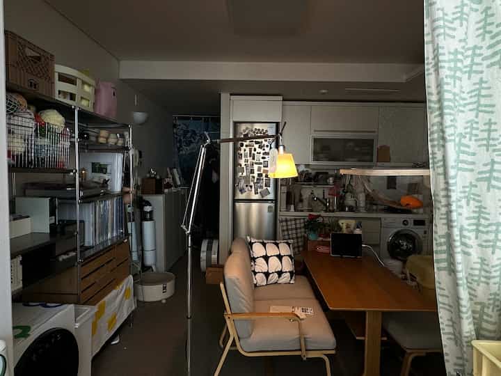 Beige and white wood-tone living room connected to kitchen featuring Artemide floor lamp, sofa, and dining table in a practical cozy space