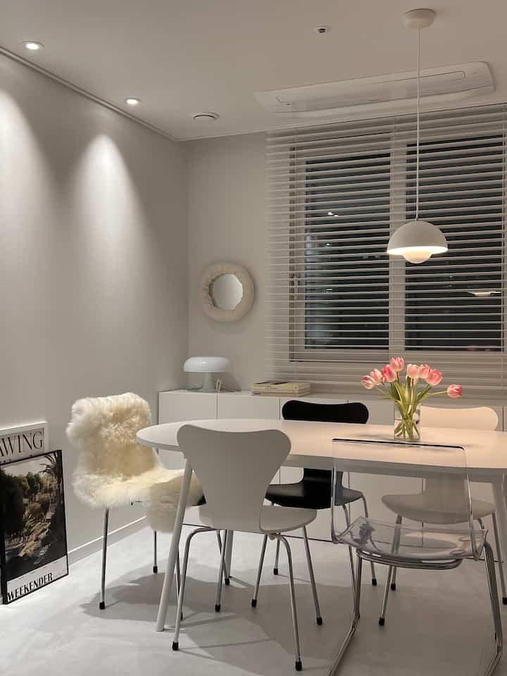 White-toned dining room featuring a 6-person dining table with diverse chairs in a simple, modern space