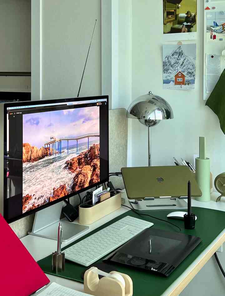 A modern home office with white and green tones featuring a desk, computer monitor, and silver dome lamp creating a clean work environment
