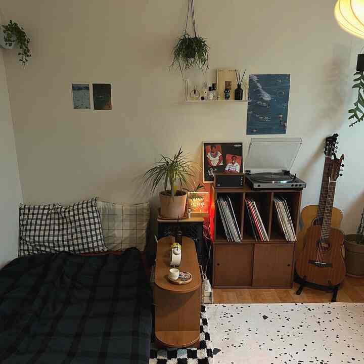 ナチュラルな色調のリビング兼寝室、ベッドと木製家具、レコードプレーヤーとギターが調和した雰囲気のあるインテリア