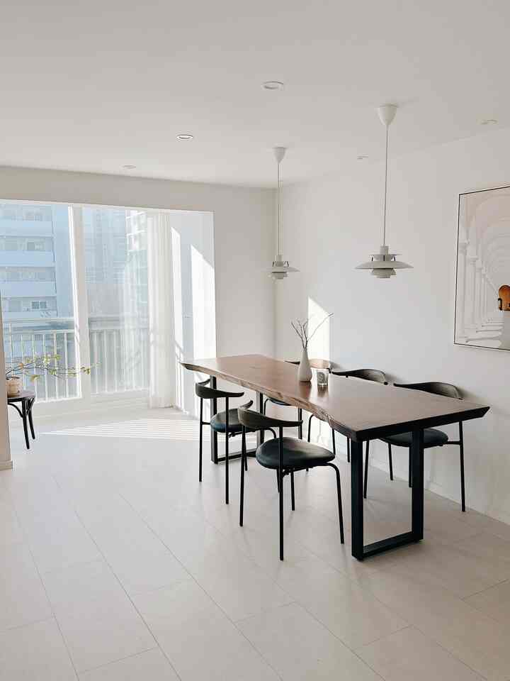 Modern dining room with white and natural wood tones, featuring a long table and pendant lights in a bright, clean space