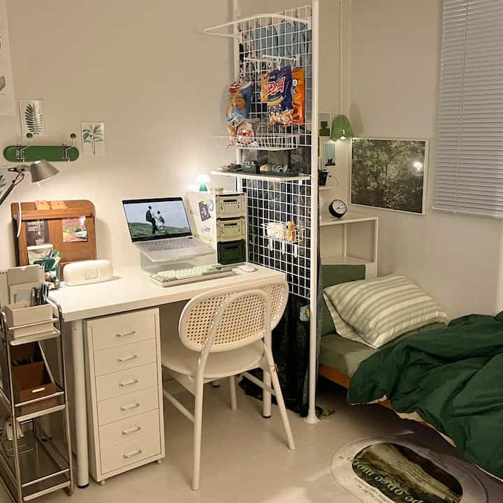 White and green toned compact bedroom and remote work space featuring a white desk, chair, room divider, and bed in a tidy arrangement