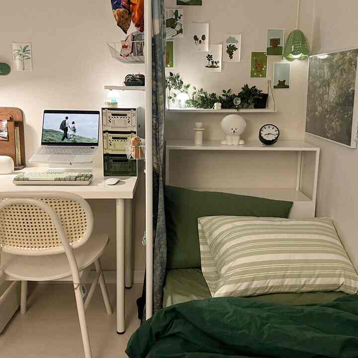 White and green toned studio bedroom featuring a desk, plants, clock, and lamps in a cozy setting