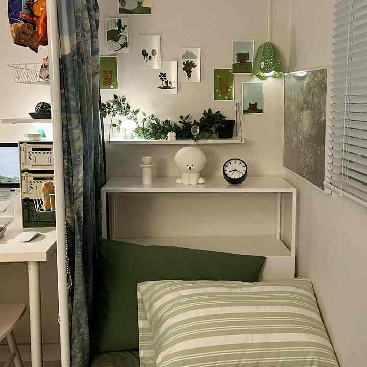 White and green toned small bedroom featuring a desk, cushions, and wall lamp with a cozy atmosphere
