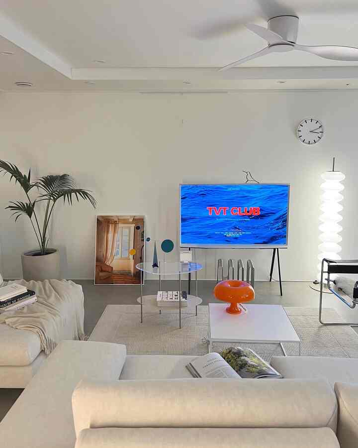 White and beige toned living room featuring modern sofas, art poster, stand TV, and floor lamp with minimalist atmosphere