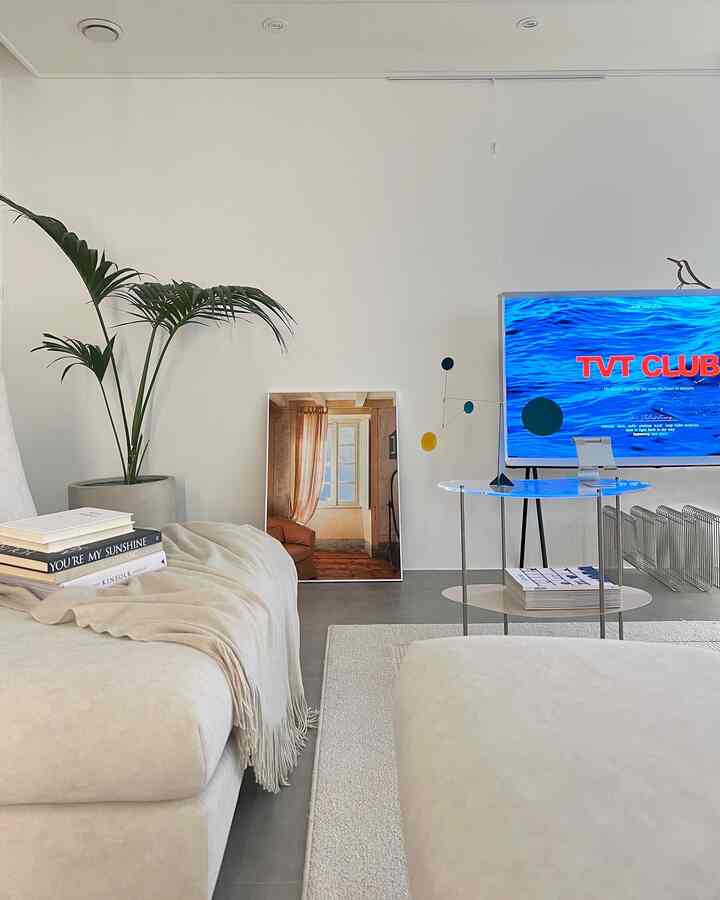 Bright white-toned modern living room featuring cream sofa, glass table, and TV for a neat atmosphere