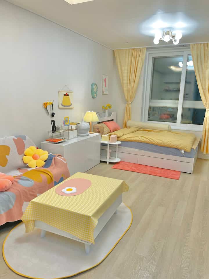 A cozy living room featuring yellow curtains and bedding, white furniture, and soft decorative elements creating a warm atmosphere