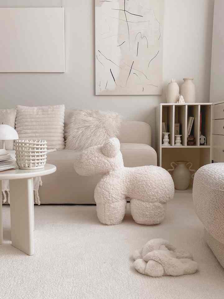 Ivory and beige toned living room featuring soft fabric sofa, plush rug, abstract wall art, and organized shelving creating a cozy atmosphere