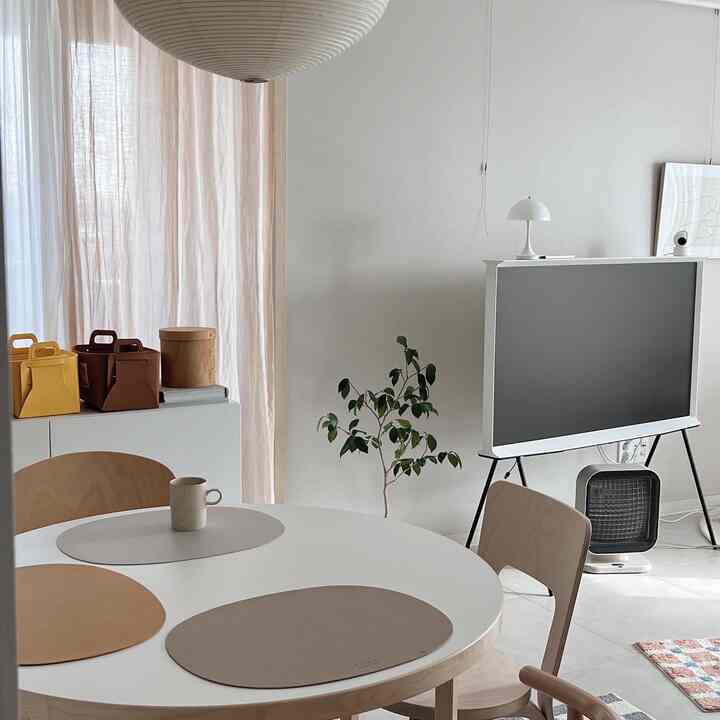 White and beige toned living room featuring a round dining table, wooden chairs, a TV, and a plant in a clean setting
