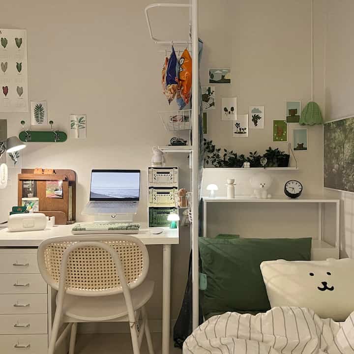 A cozy single household bedroom and home office space in white and green tones, featuring a partition and wall art decorations