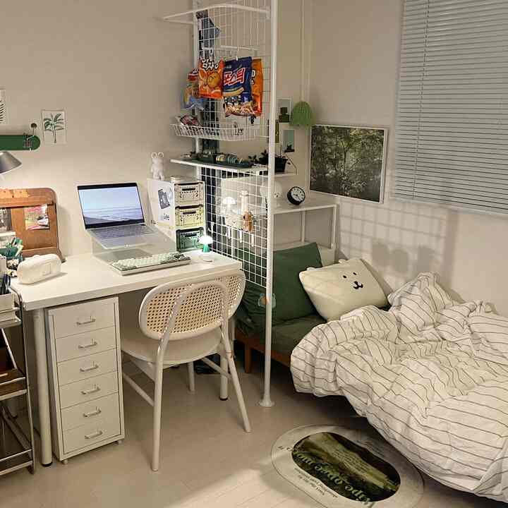ホワイトとグリーンの落ち着いた色調のコンパクトな寝室、整ったデスクと収納棚、きちんとしたベッドが配置された雰囲気のあるインテリア