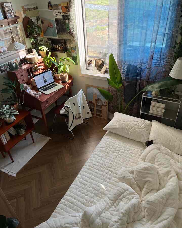白と木目調の調和が美しい寝室、窓際の机と植物、布団の上にいる二匹の猫が落ち着いた雰囲気を演出