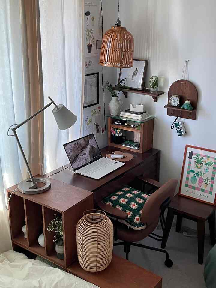 A cozy studio home office with white walls and curtains, wood tone furniture, and a bamboo pendant light
