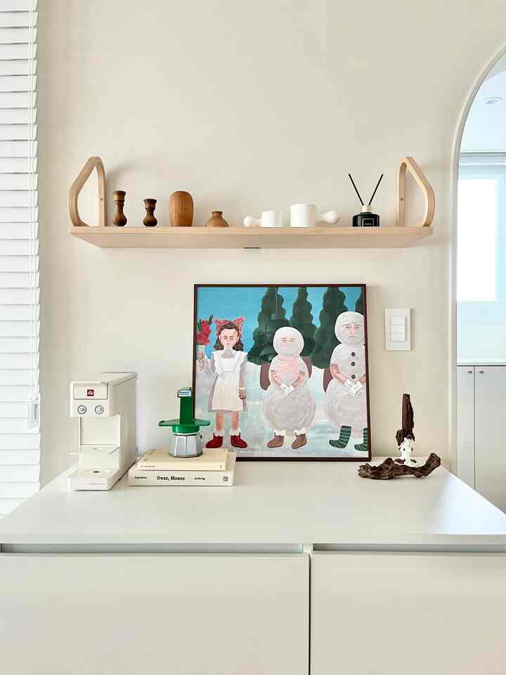 Minimal kitchen space in white and wood tones featuring an Artek wall shelf, Illy coffee machine, and diffuser with a clean atmosphere