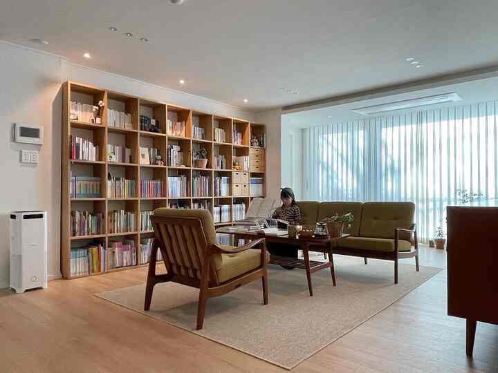 Natural wood-toned living study with large bookshelf and olive sofa arranged in a cozy atmosphere