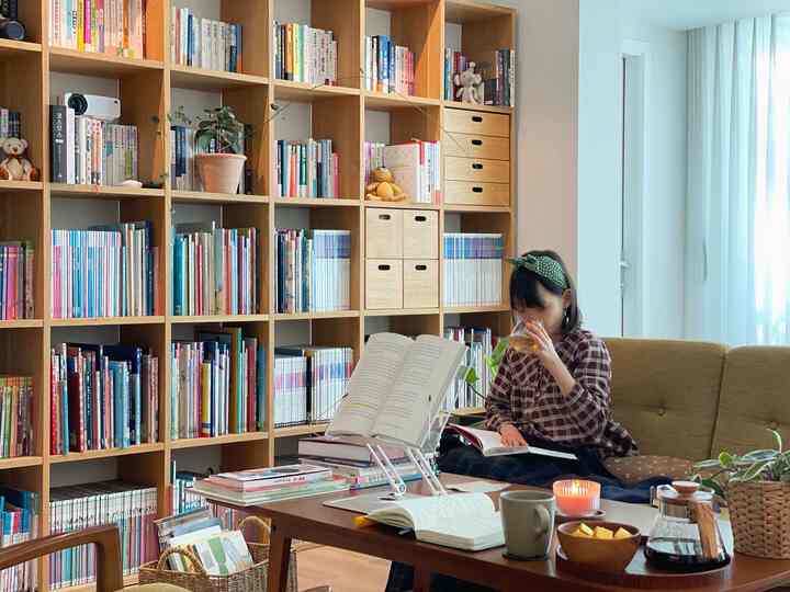 Warm brown wood-tone living room with white curtains, featuring bookshelves and a reading stand creating a peaceful reading area