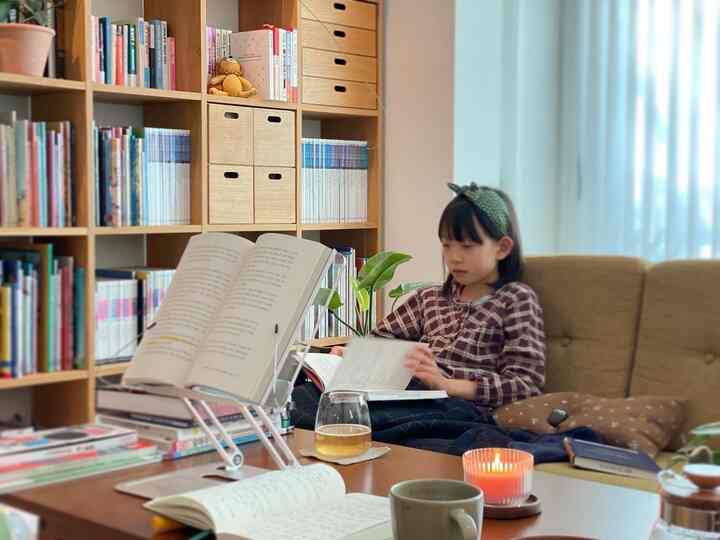 A cozy study space with warm wood tones and white curtains, featuring a child reading on an olive sofa