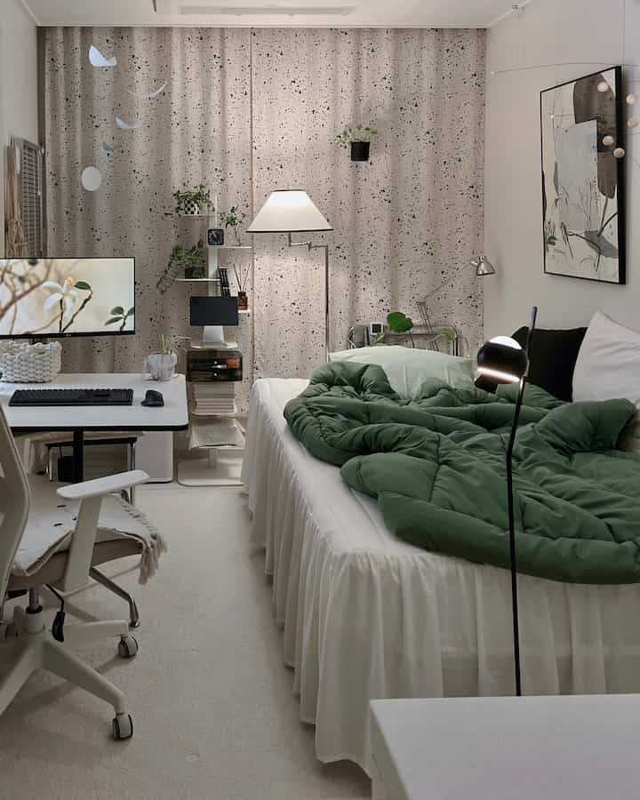 A white and green toned studio apartment bedroom featuring bed and desk, cozy natural home office space