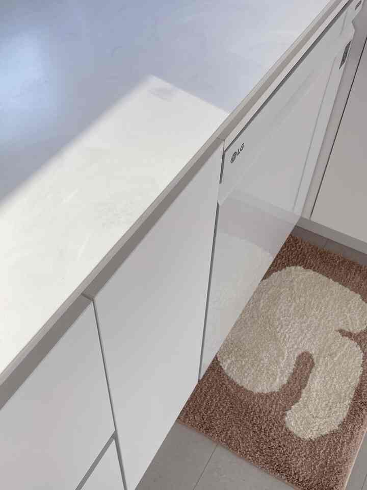 明るいホワイトトーンのキッチン、LGの食器洗浄機とアドニスのバスマットが配置された清潔で明るい空間