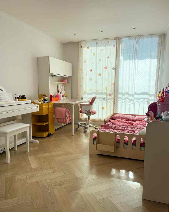 ピンクと木目調の調和が取れた子供部屋、デスカーの机と子供用ベッドが配置された明るく居心地の良いインテリア